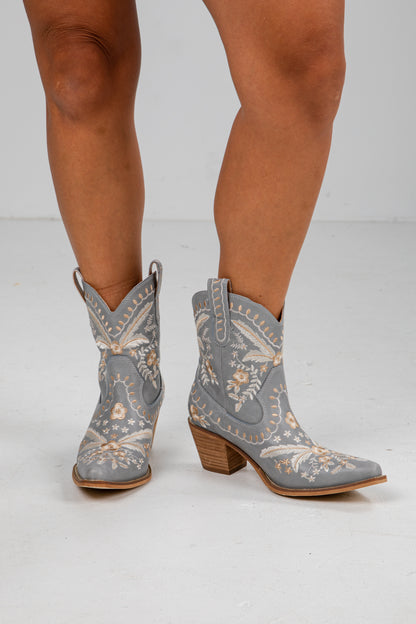 Gray embroidered cowboy boots worn by a person on a white background
