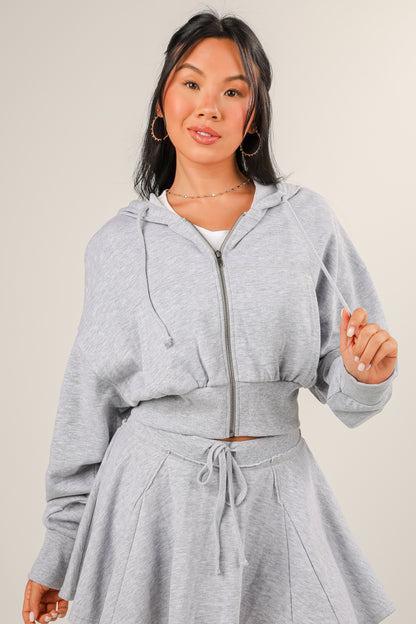 Woman wearing a gray hoodie and skirt set on a plain background