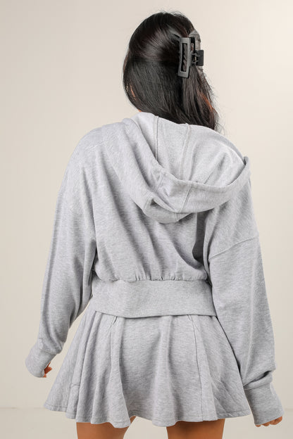 Person wearing a gray hoodie and skirt set against a plain background