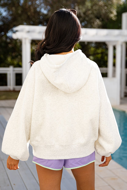 Person wearing a white hoodie and purple shorts standing by a poolside.