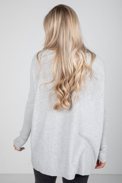 Person wearing a light gray cardigan with long blonde hair on a plain background