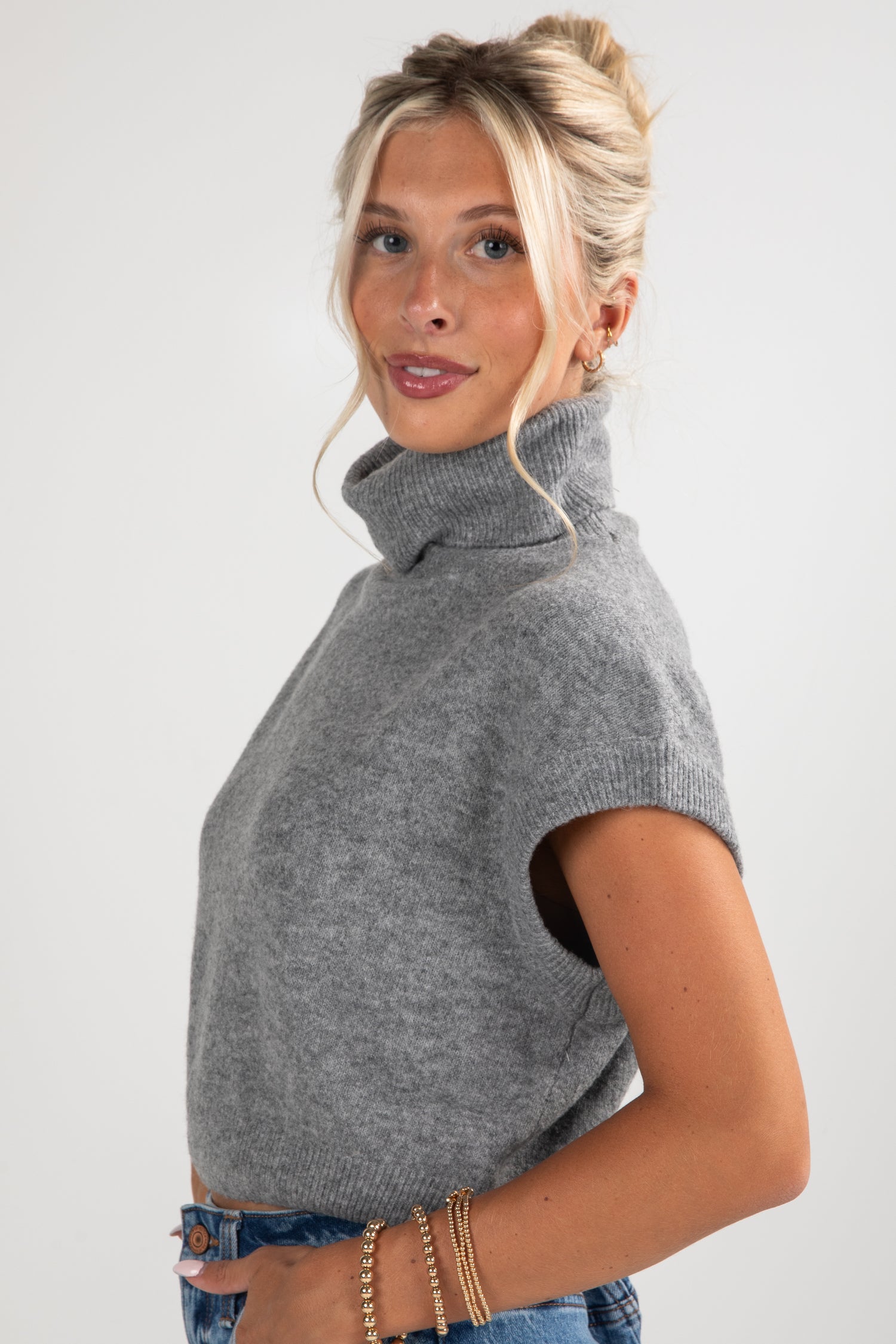 Woman wearing a gray sleeveless sweater against a white background