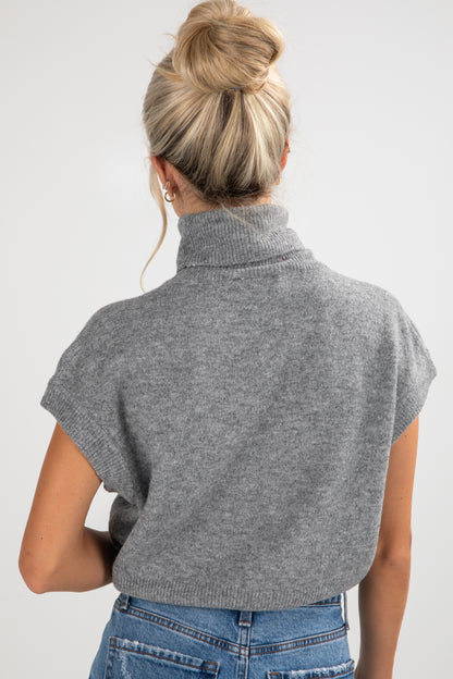 Person wearing a gray turtleneck sweater over a blue top on a white background