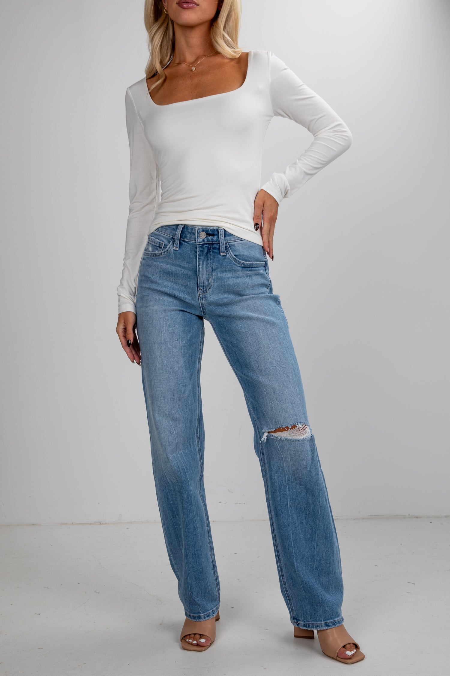 Woman wearing a white long-sleeve top and blue jeans on a plain background