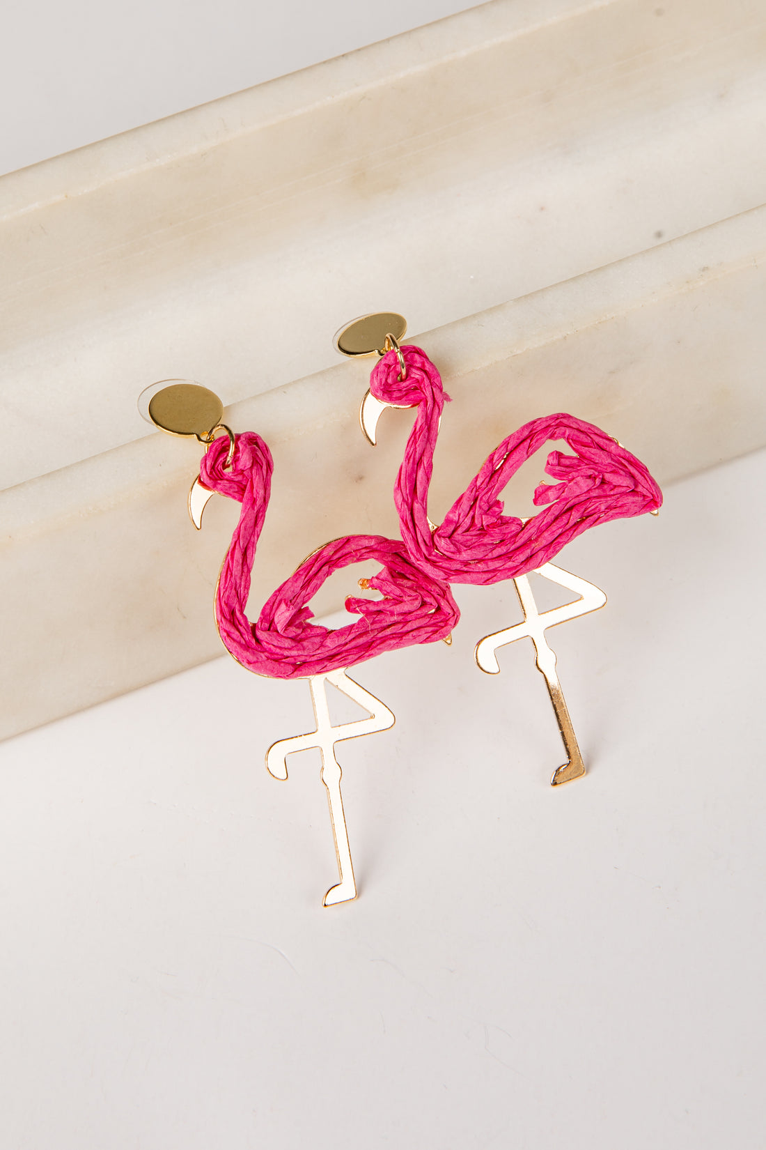 Flamingo-shaped earrings with pink feathers and gold legs on a light background