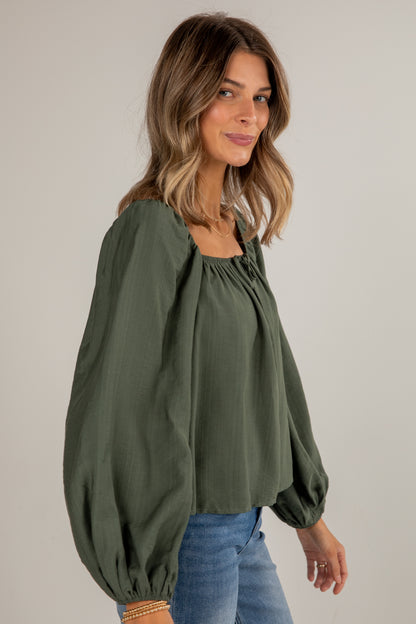Woman wearing an olive green blouse with balloon sleeves against a plain background