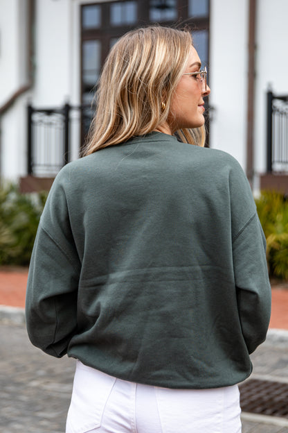 Person wearing a green sweatshirt and white pants outdoors.