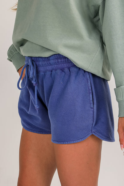 Person wearing blue shorts and a green sweatshirt on a plain background