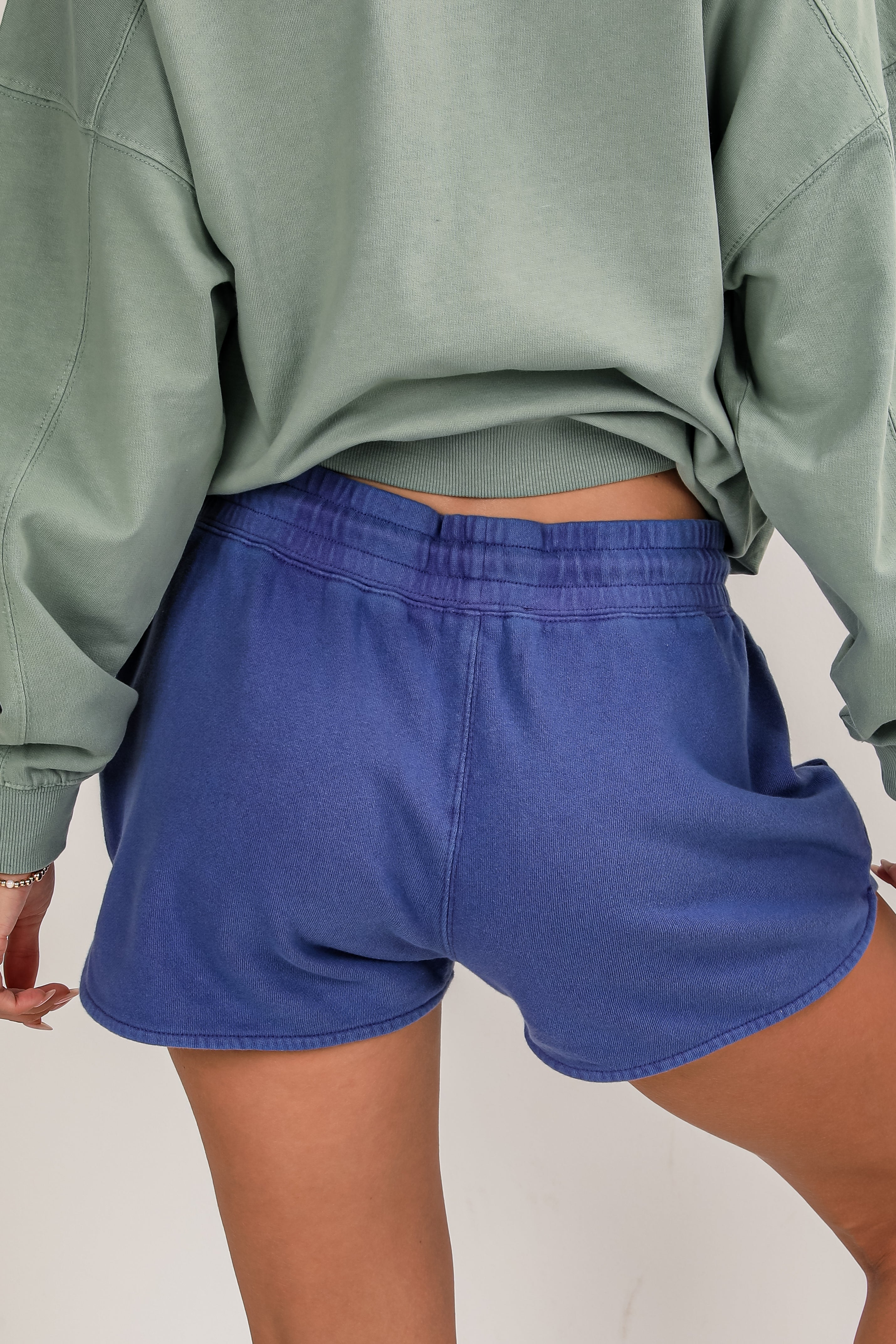 Person wearing a green sweatshirt and blue shorts on a neutral background