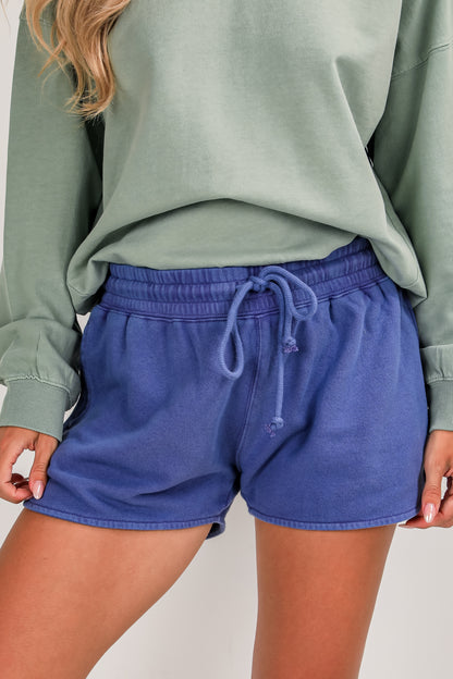 Person wearing blue shorts and a green sweatshirt on a plain background