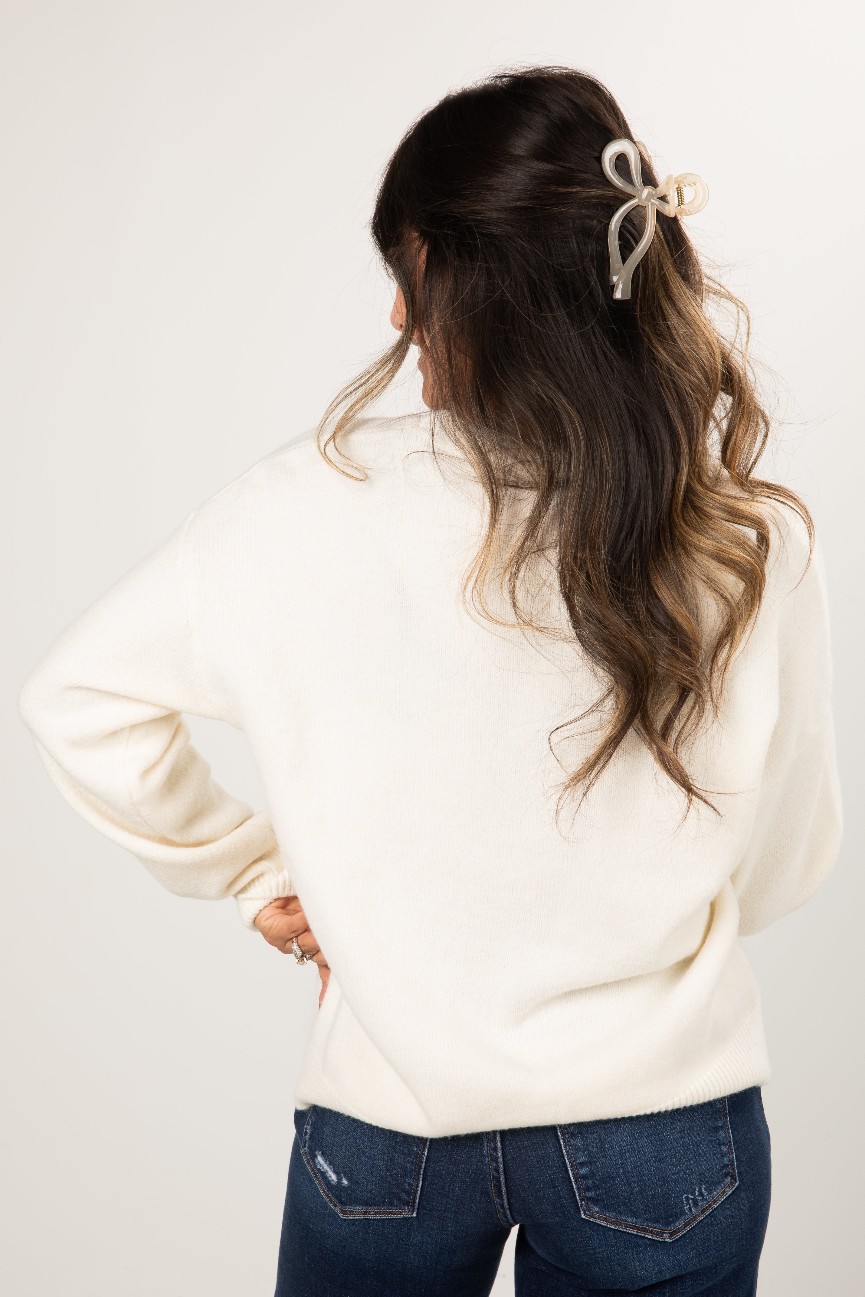 Woman with styled hair wearing a white sweater and blue jeans on a plain background