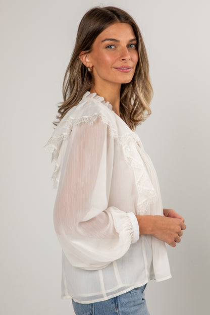 Woman wearing a white blouse with sheer sleeves against a plain background