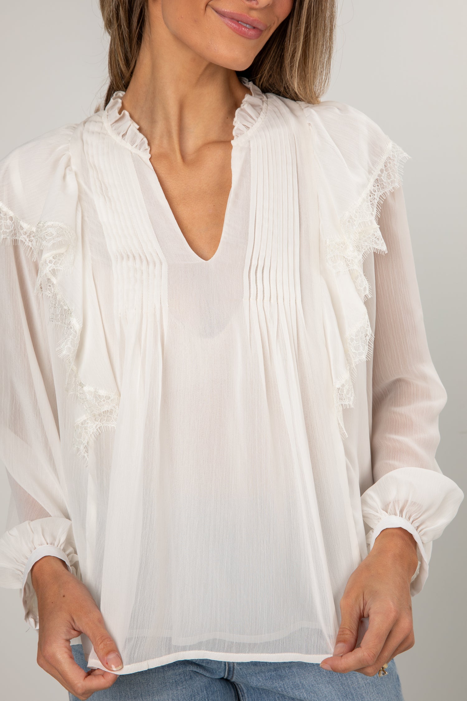 Woman wearing a white blouse with lace details on a plain background