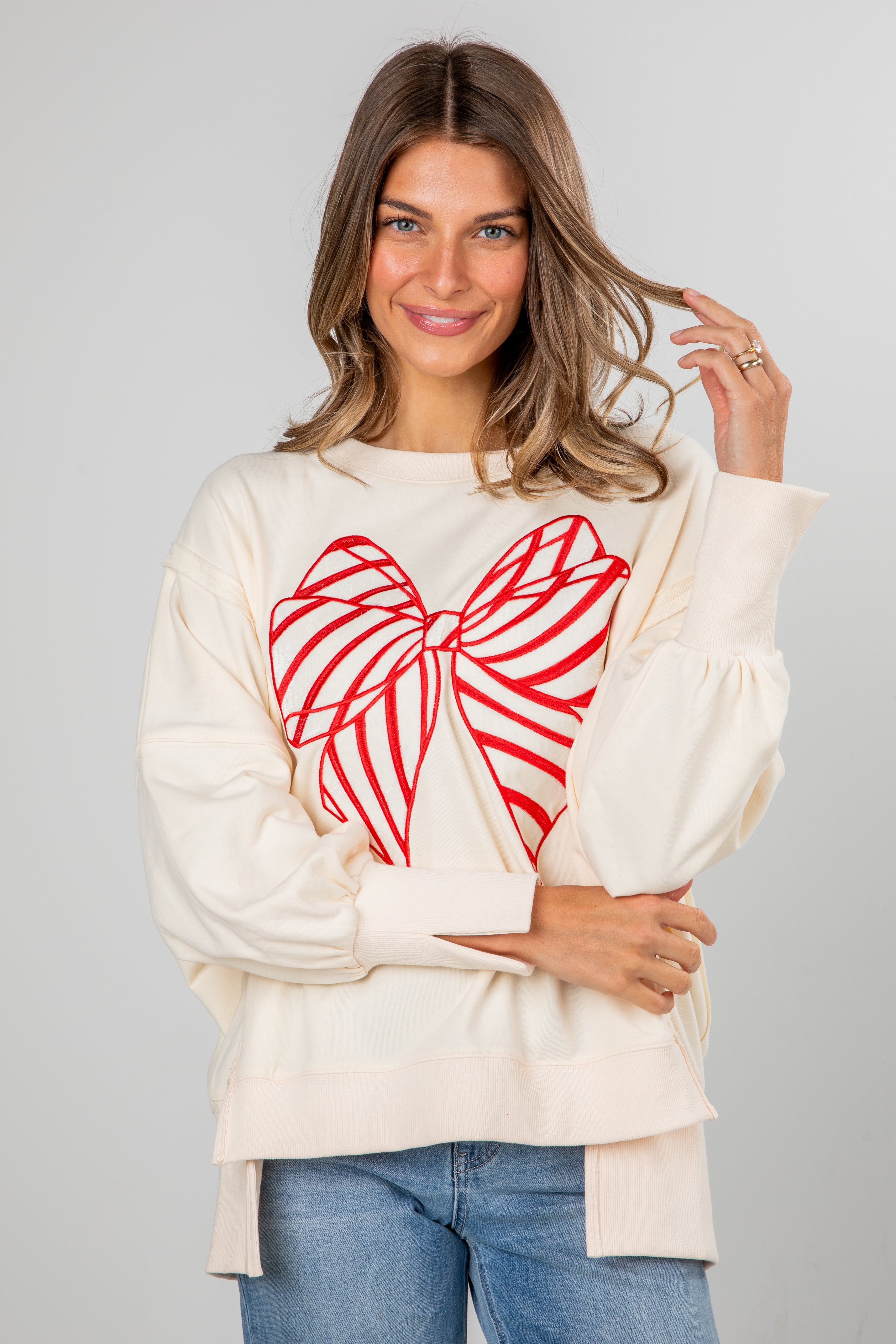 Woman wearing a cream sweater with a red heart design on a gray background