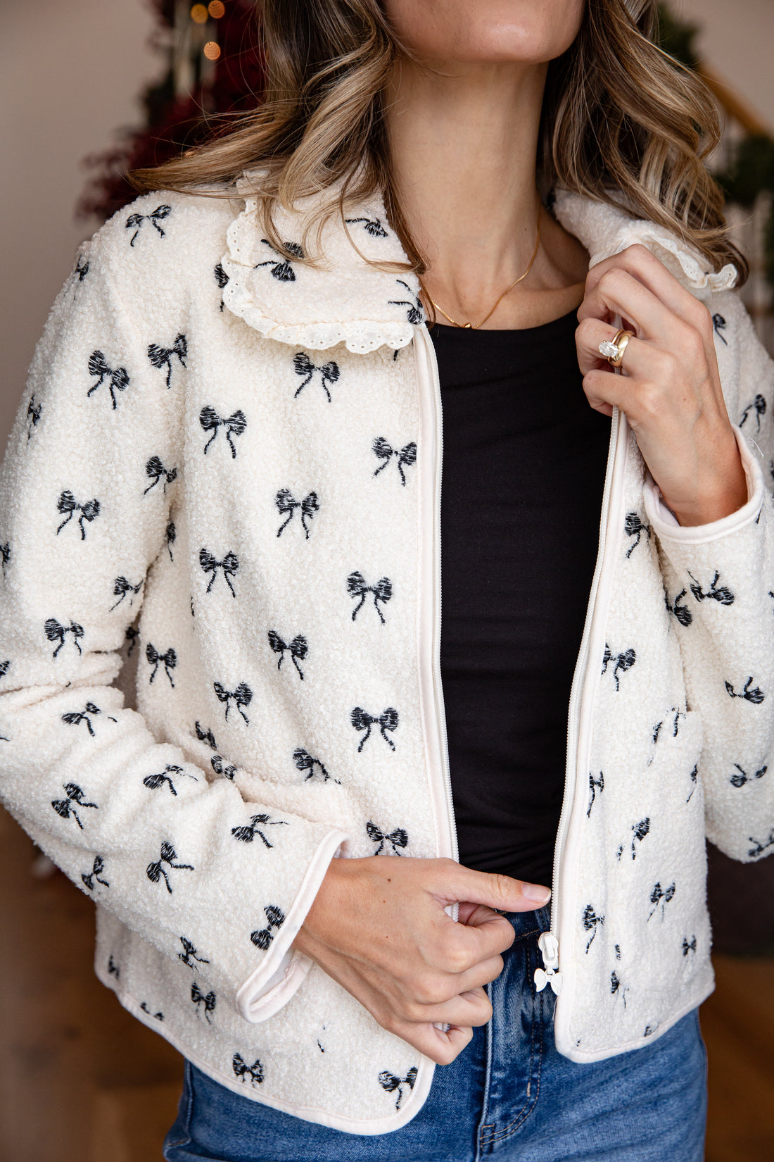 Person wearing a white jacket with black bow patterns, black top, and blue jeans.