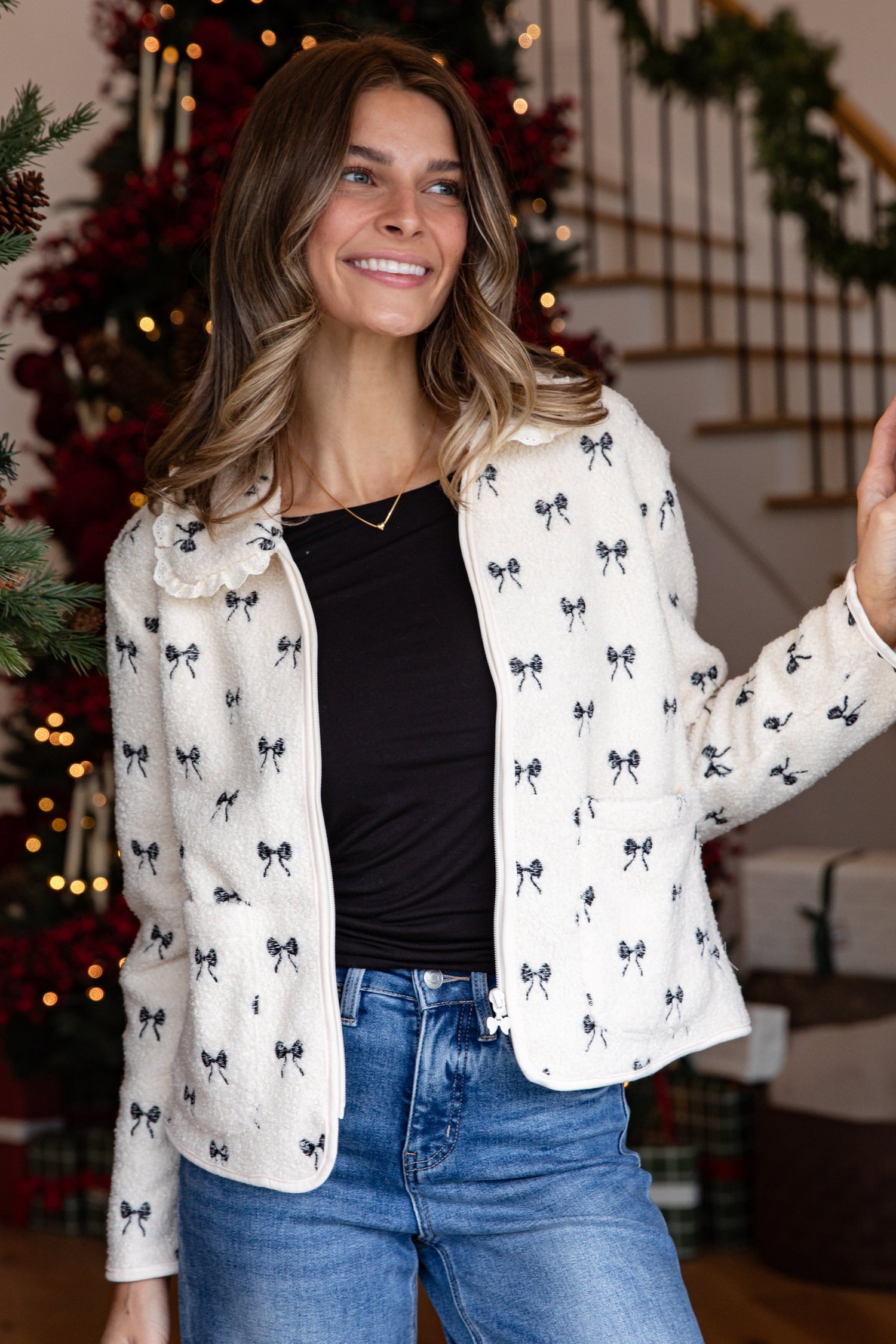 Woman wearing a white blouse with black patterns and blue jeans in a festive indoor setting.