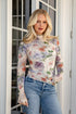 Woman wearing a floral blouse and jeans standing in front of a glass door.