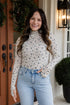 Woman wearing a floral long-sleeve top and jeans standing in front of a door.