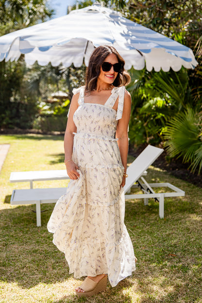 Woman in a floral dress standing under a striped umbrella in a garden setting