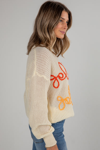 Woman wearing a cream sweater with colorful text on a plain background