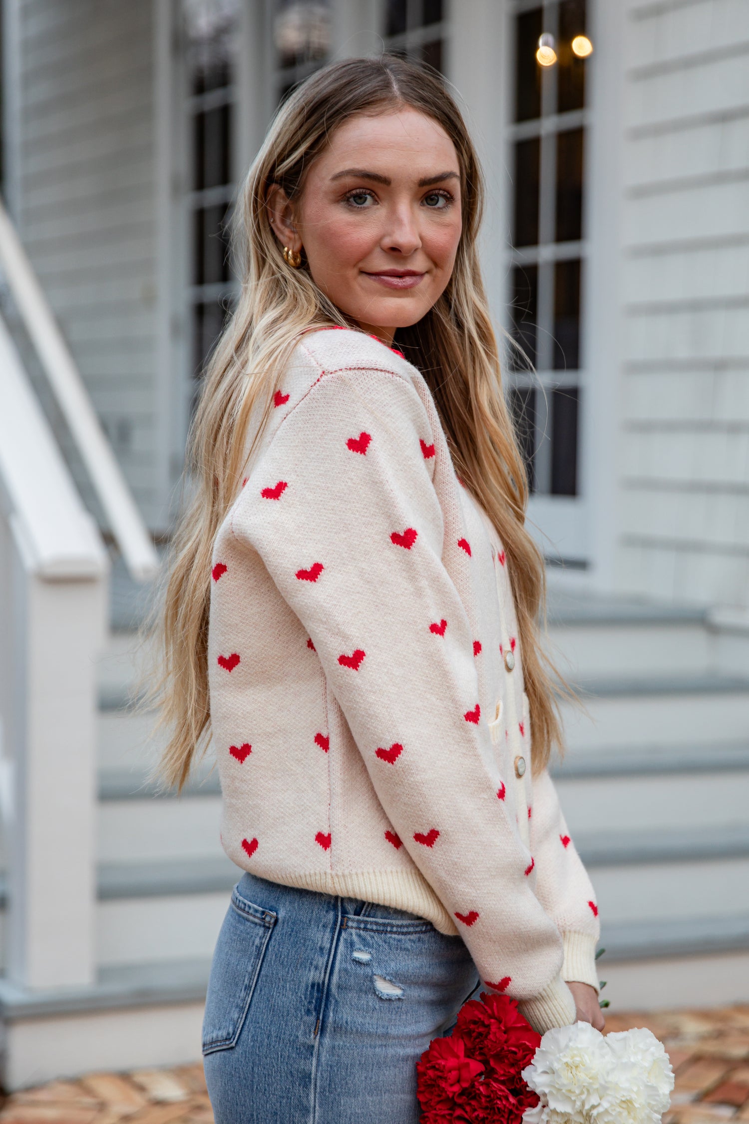 Woman wearing a cream sweater with red heart patterns, standing outdoors.