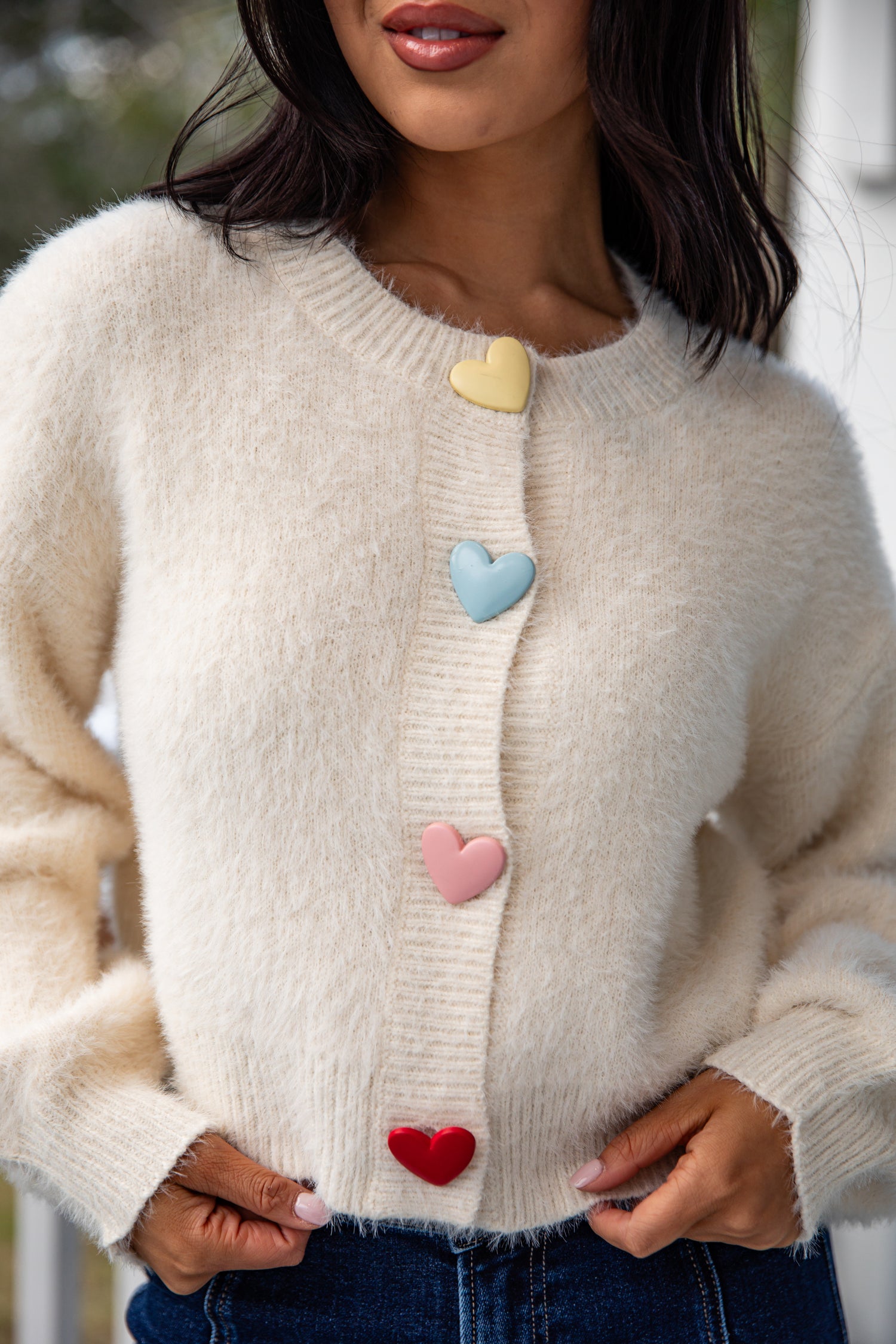 Beige sweater with colorful heart buttons worn by a person.
