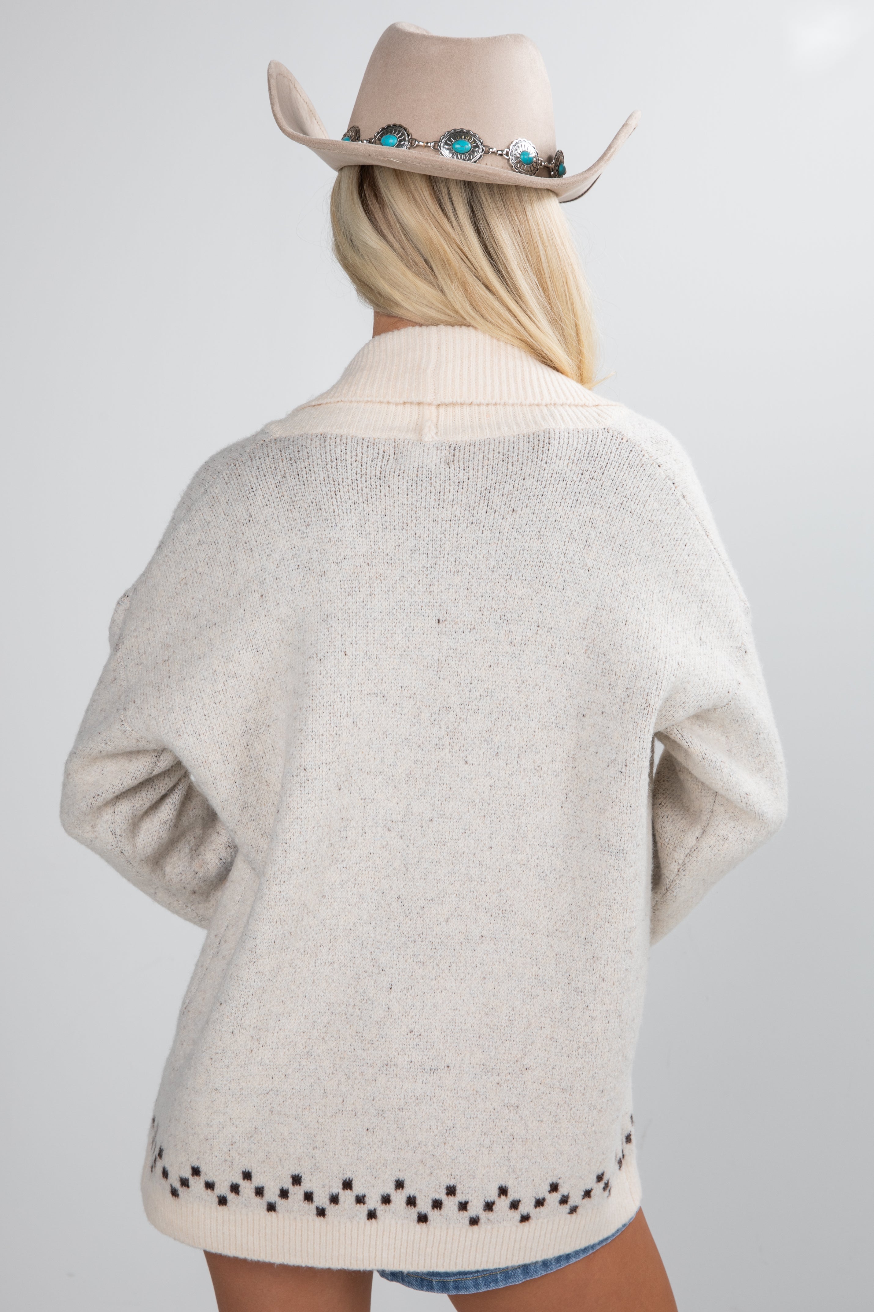 Person wearing a beige sweater and cowboy hat on a plain background