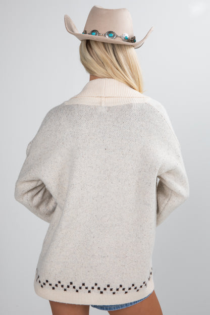 Person wearing a beige sweater and cowboy hat on a plain background