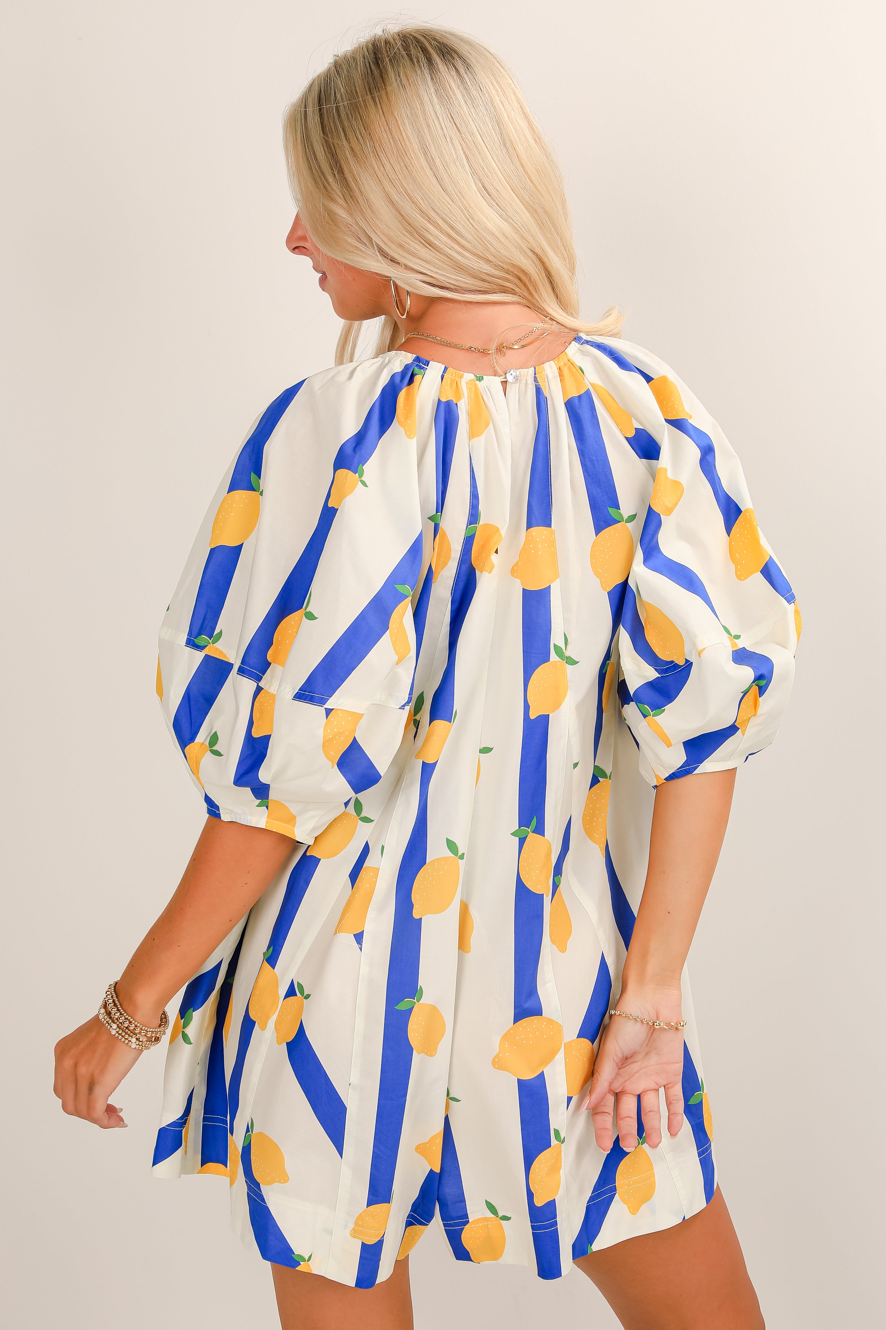Woman wearing a dress with lemon and blue stripe pattern on a beige background