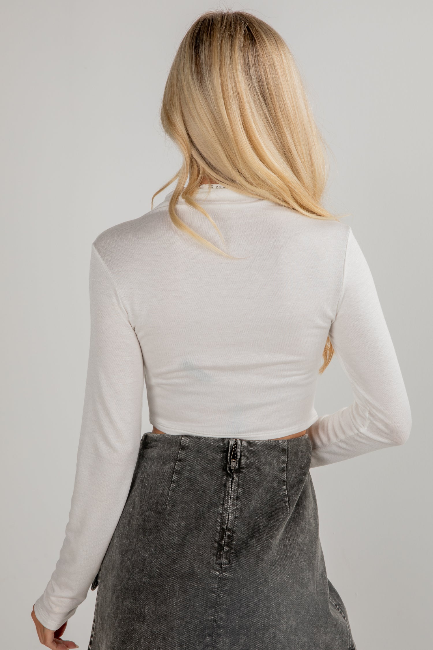 Person wearing a white long-sleeve top and gray skirt on a plain background