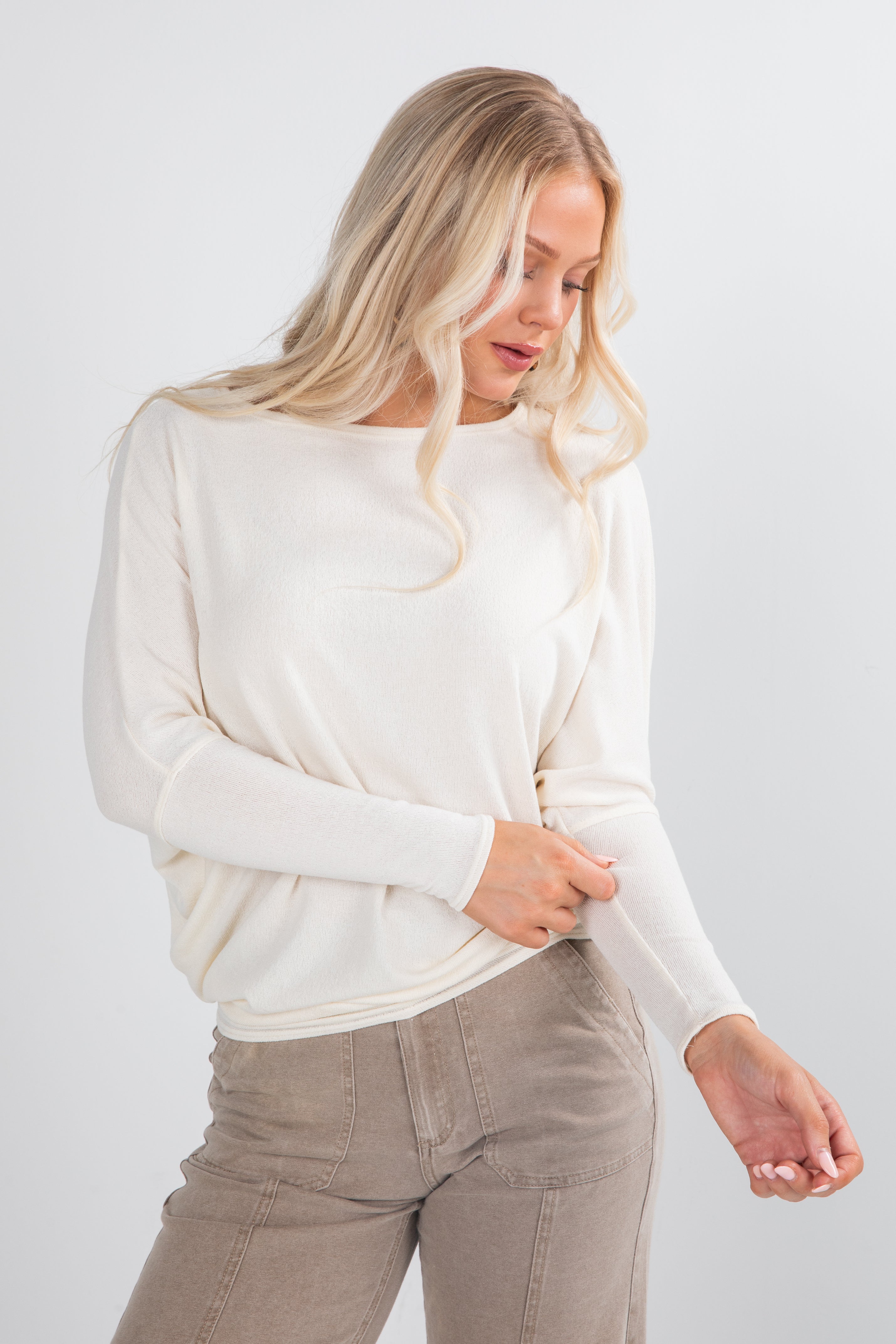 Woman wearing a white sweater and beige pants on a light gray background