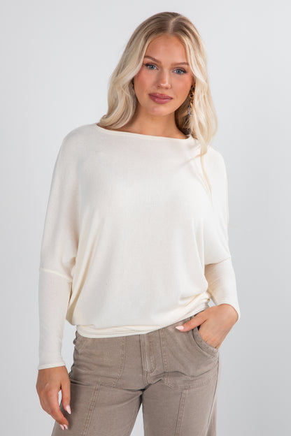 Woman wearing a white sweater and beige pants against a plain background