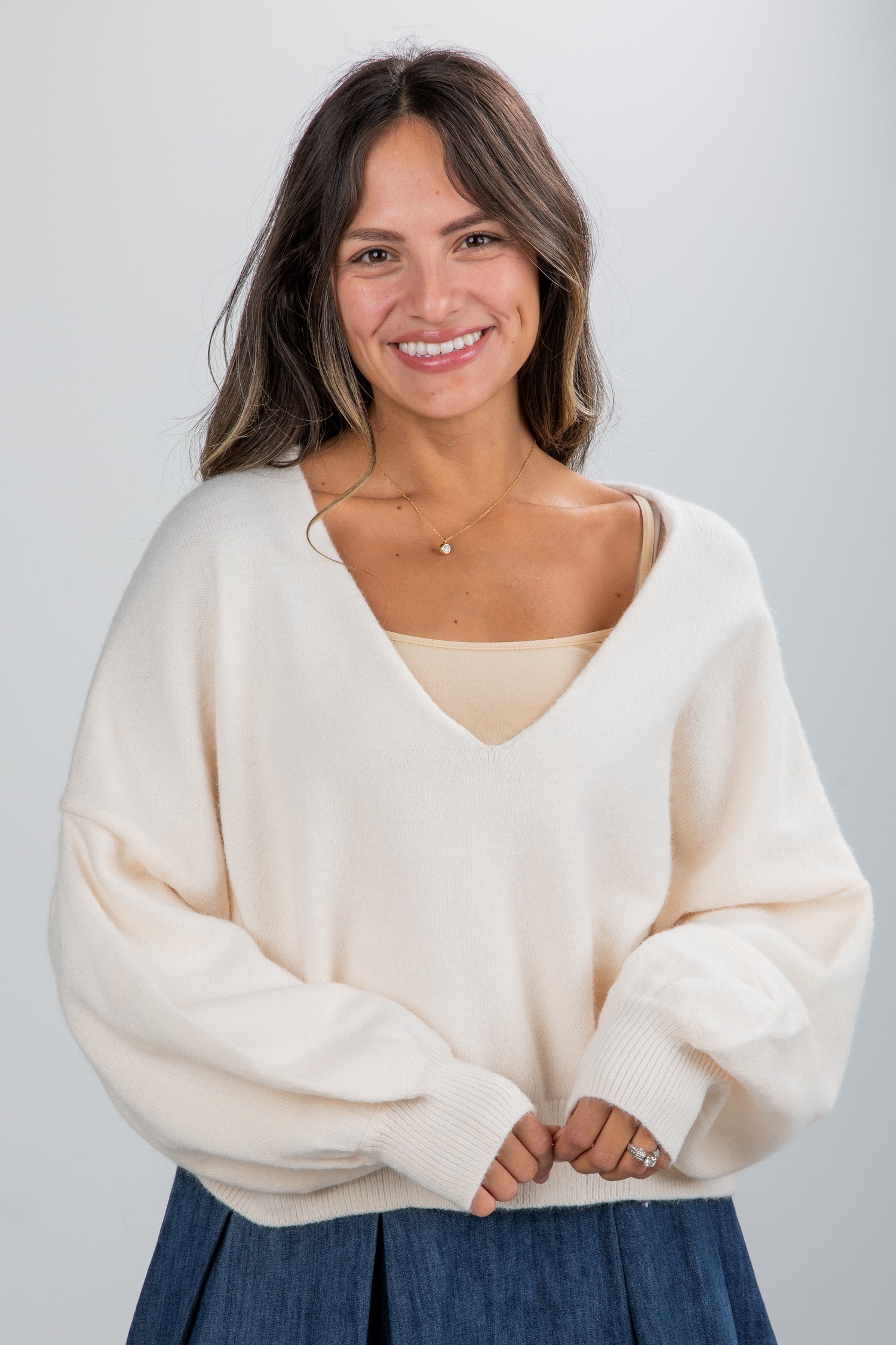 Woman wearing a cream sweater and blue skirt against a plain background