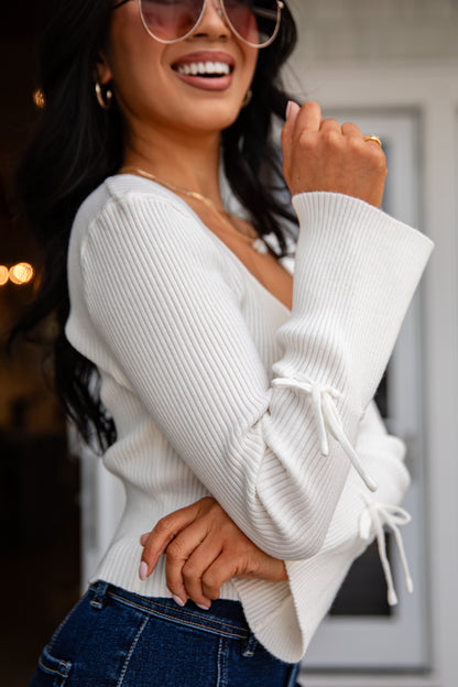 Woman wearing a white ribbed sweater with ruffled sleeves and blue jeans.