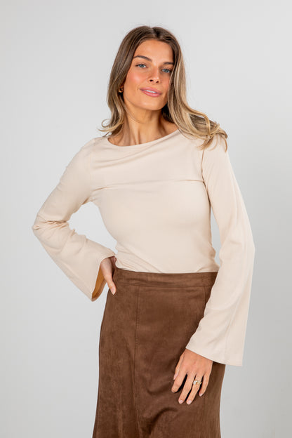 Woman wearing a beige long-sleeve top and brown pants against a plain background