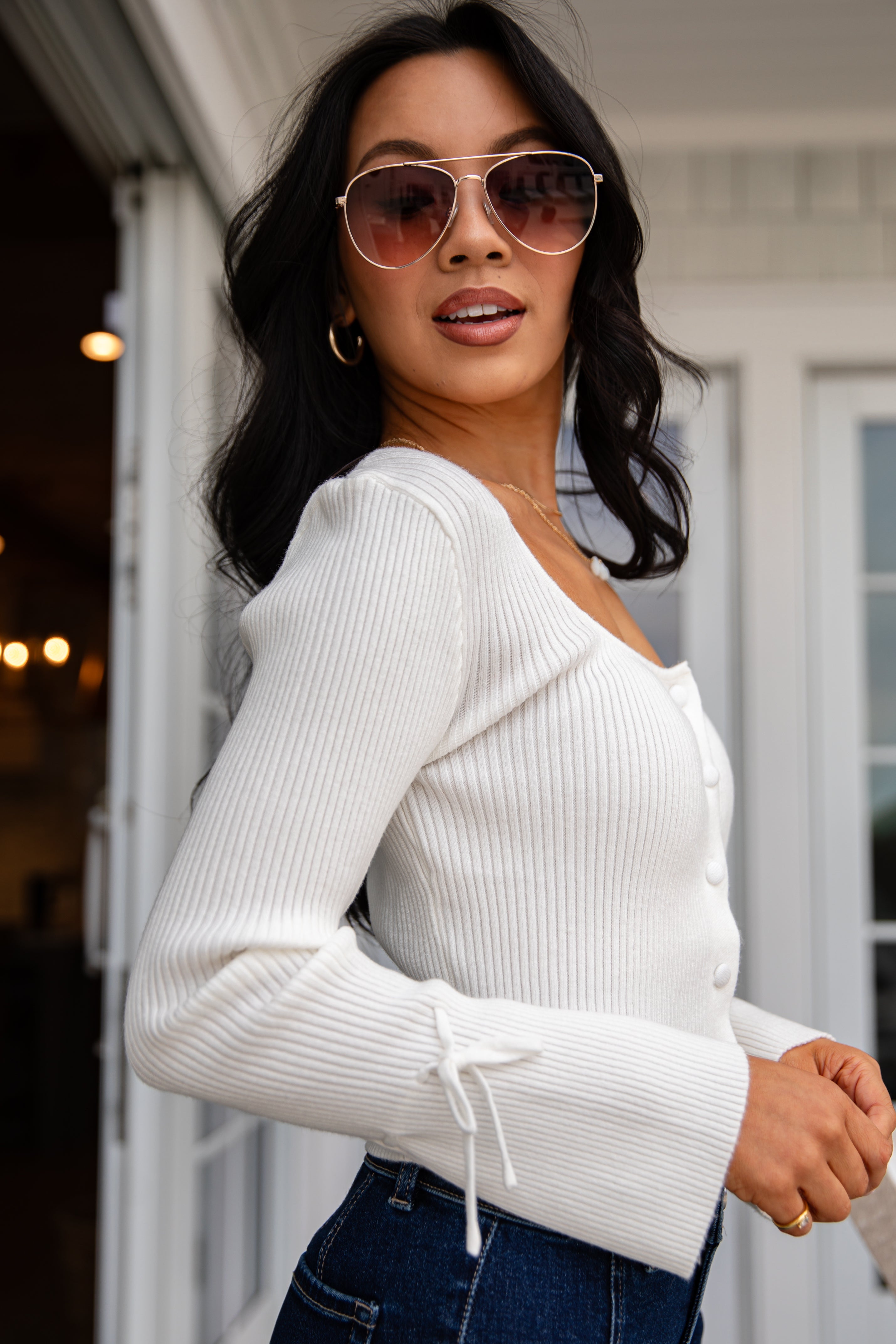 Woman wearing a white ribbed sweater and sunglasses outdoors.