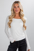 Woman wearing a white long-sleeve top and black pants against a plain background