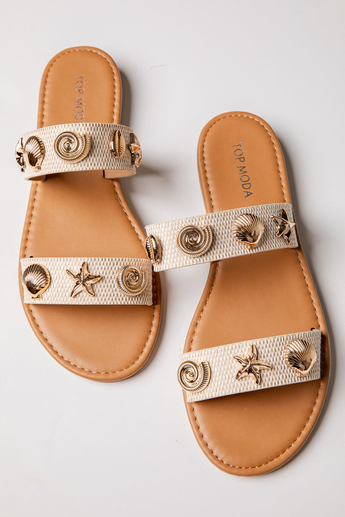 Pair of tan sandals with decorative straps featuring shells and stars on a light gray background.