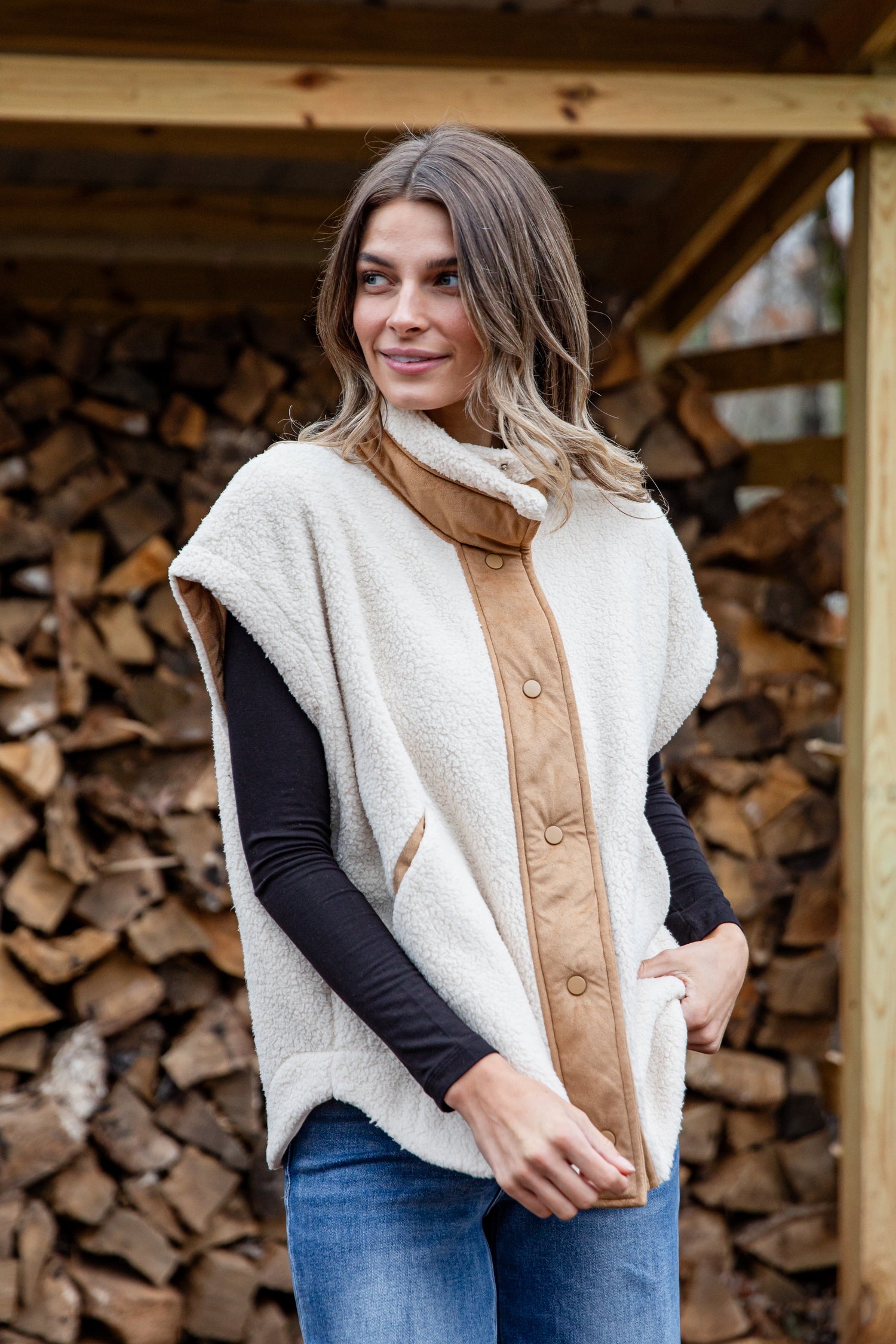 Woman wearing a cream-colored poncho with a brown interior against a wooden background.