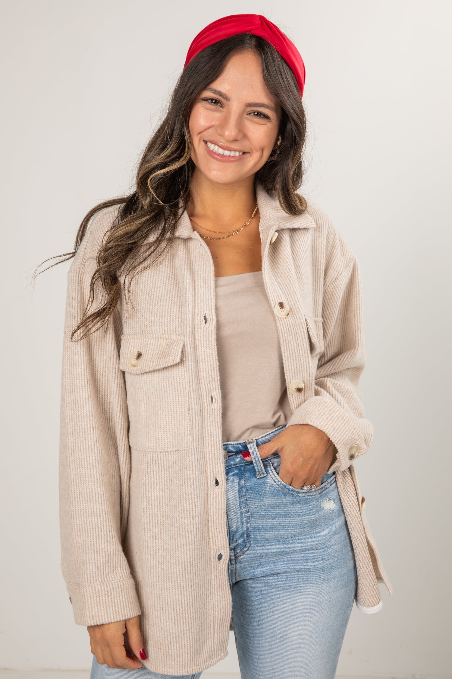 Woman wearing a beige corduroy jacket, red headband, and blue jeans against a plain background