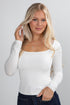 Woman wearing a white long-sleeve top against a plain background