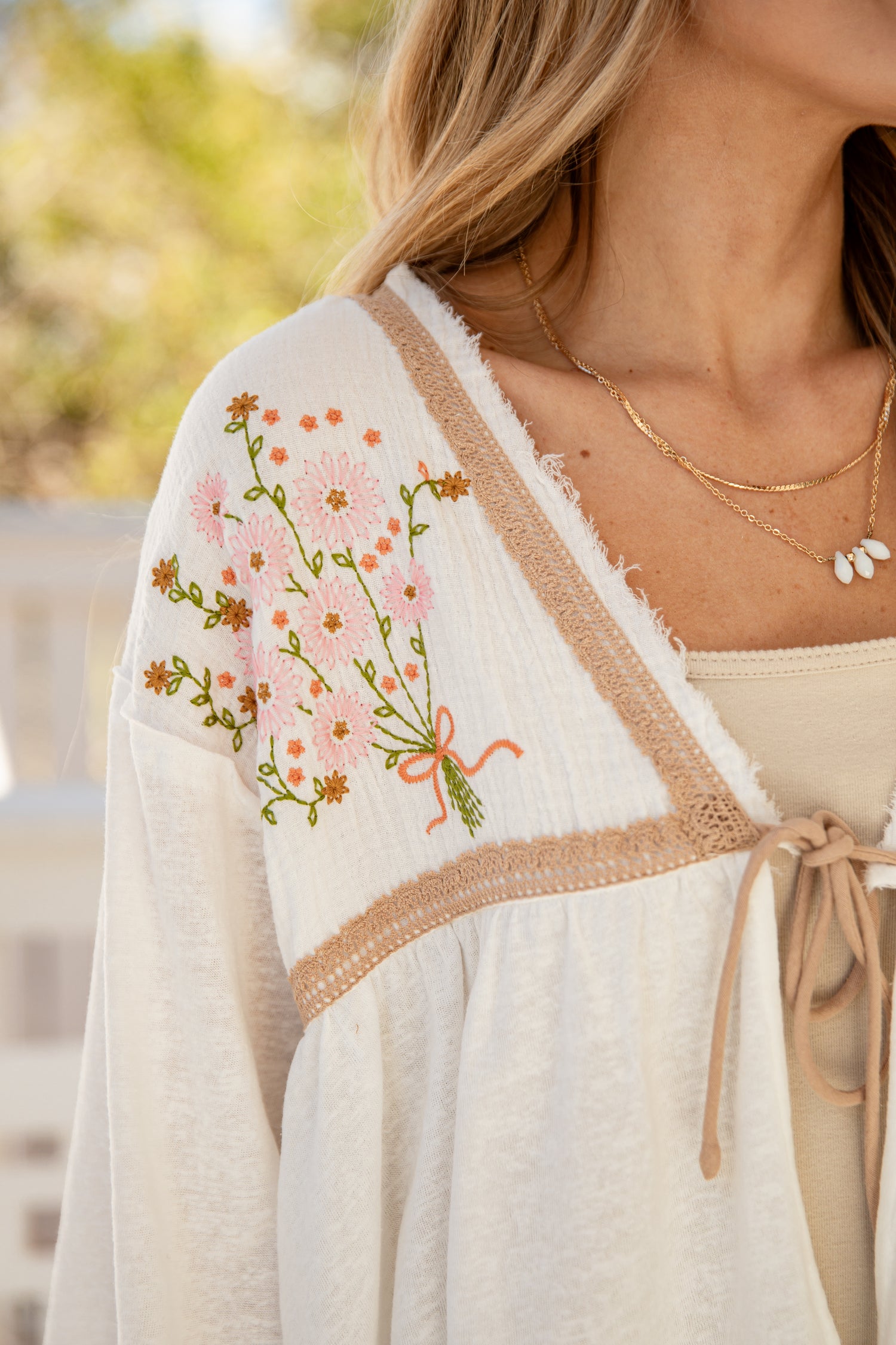Woman wearing a white embroidered cardigan with floral designs outdoors.