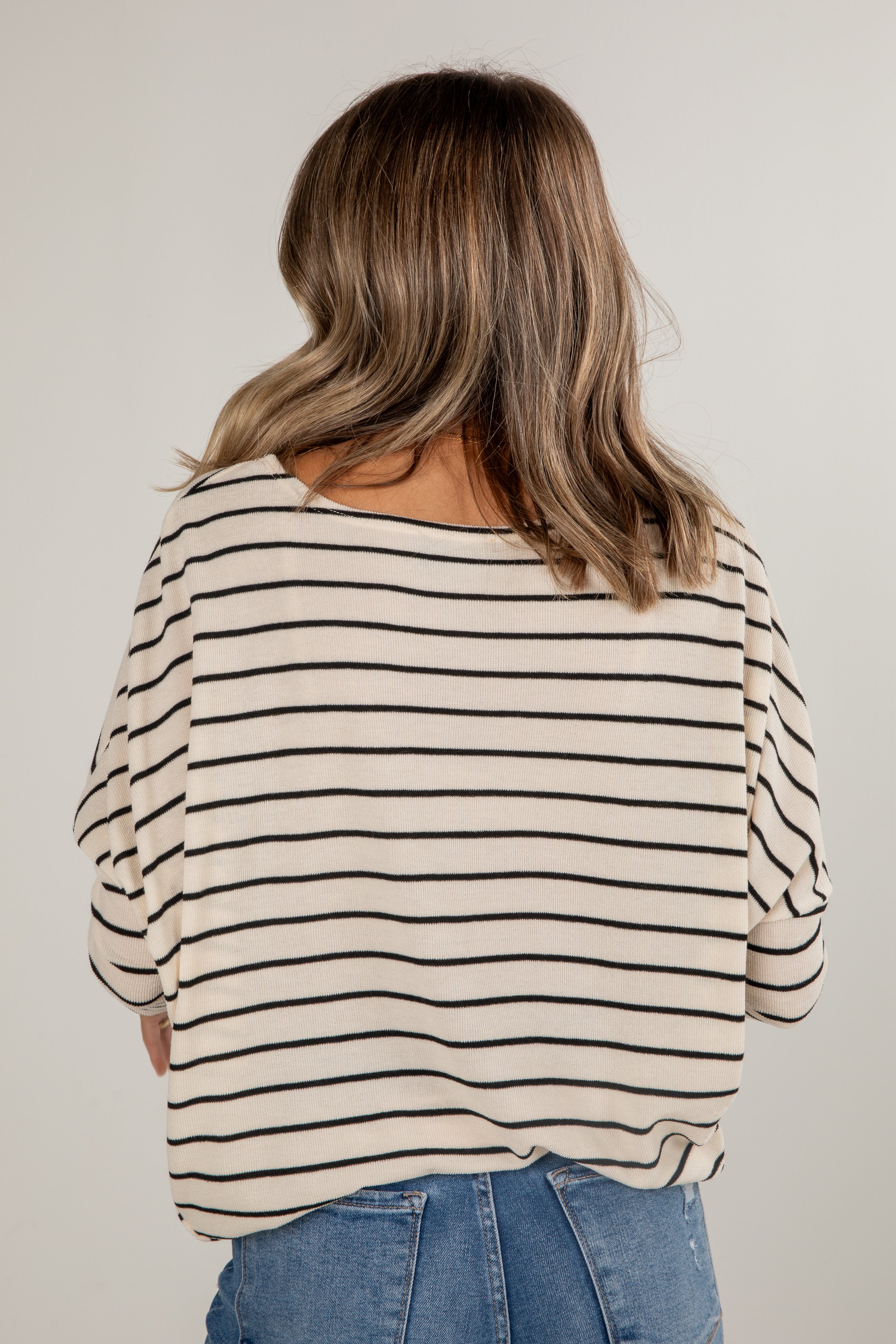 Person wearing a striped shirt and jeans against a plain background