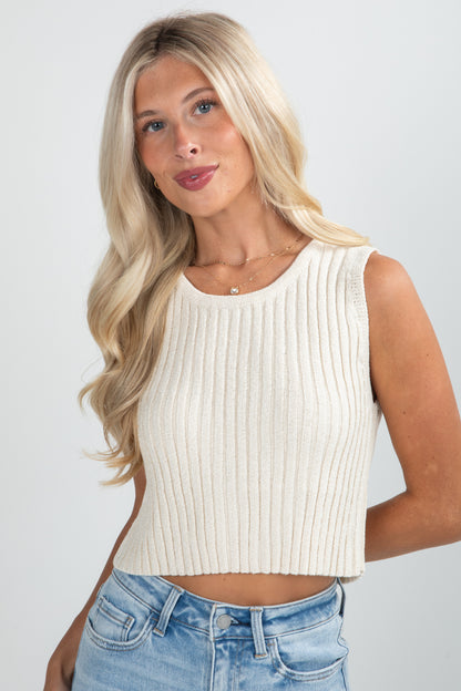 Woman wearing a white ribbed tank top and blue jeans against a plain background