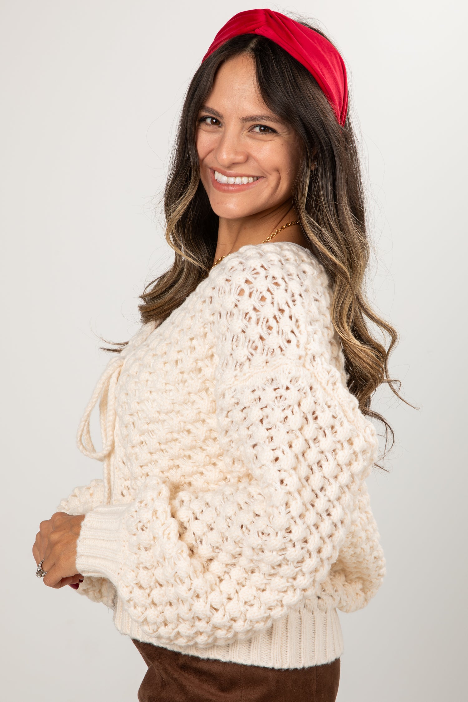 Woman wearing a white chunky knit sweater and red headband against a plain background