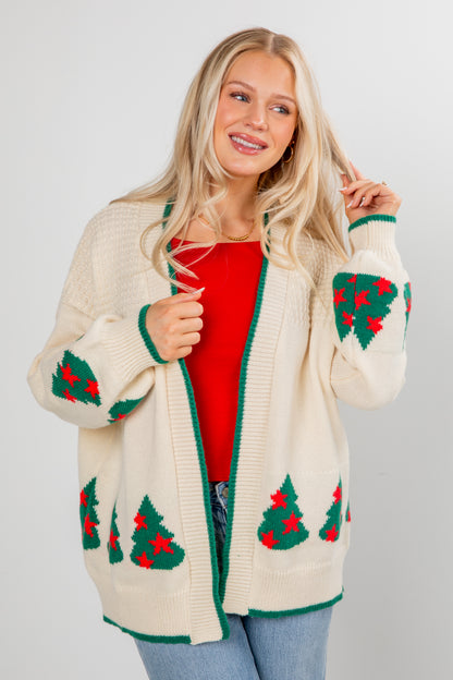 Woman wearing a cream cardigan with Christmas tree patterns on a plain background