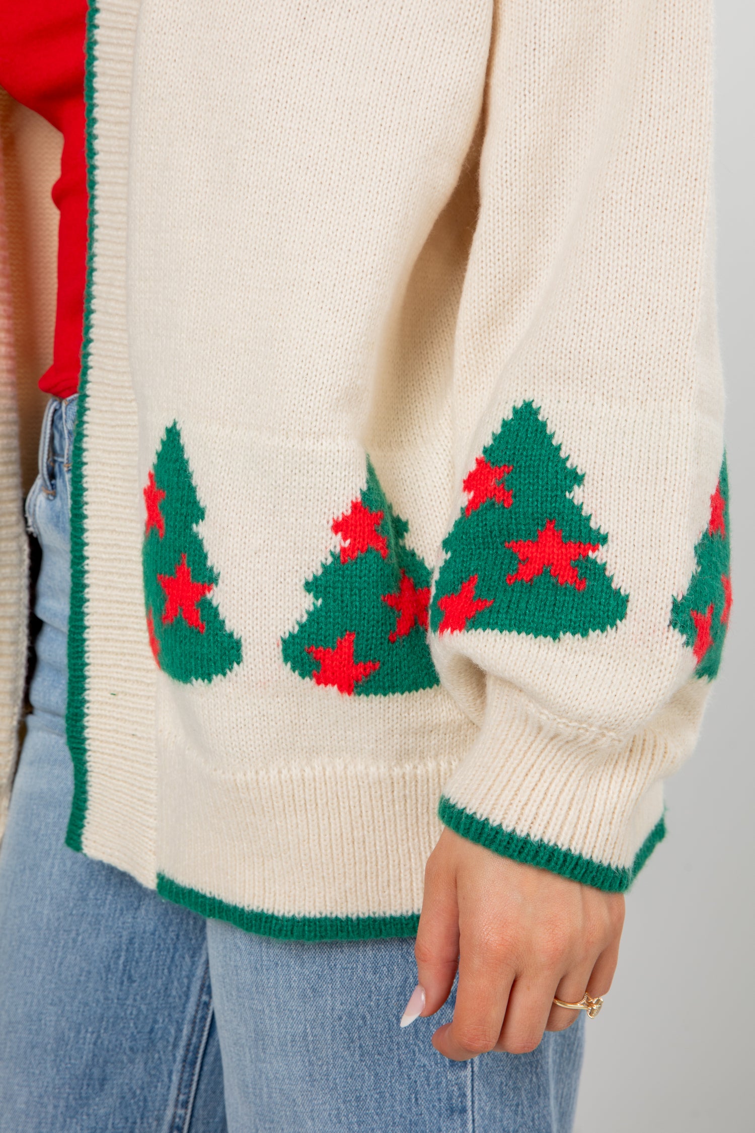Close-up of a cream sweater with green Christmas tree patterns and red stars on a neutral background.