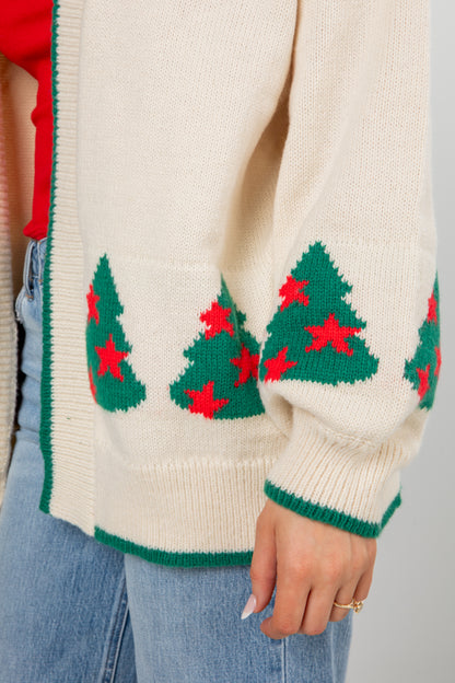 Close-up of a cream sweater with green Christmas tree patterns and red stars on a neutral background.