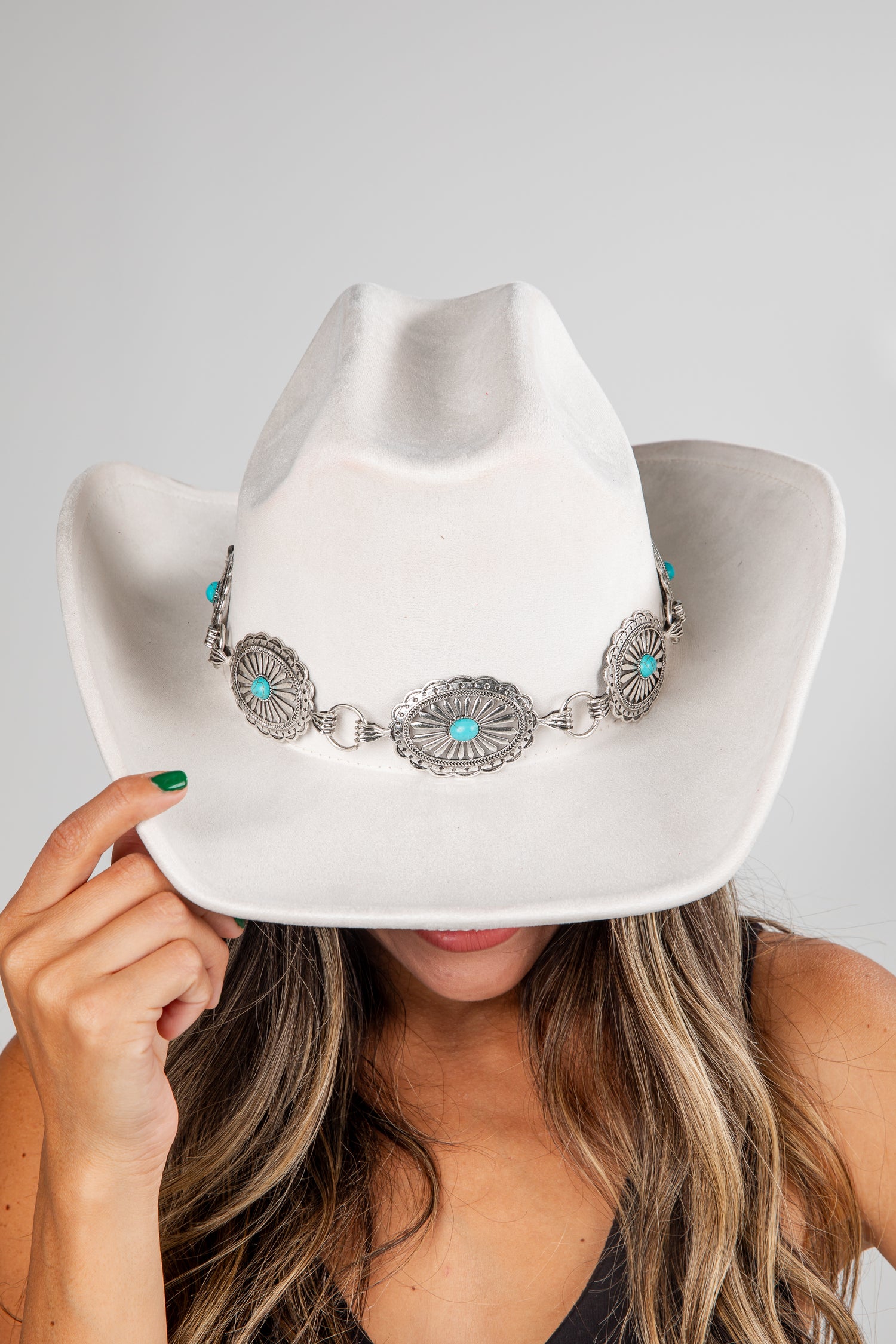 White cowboy hat with decorative band held by a person against a gray background