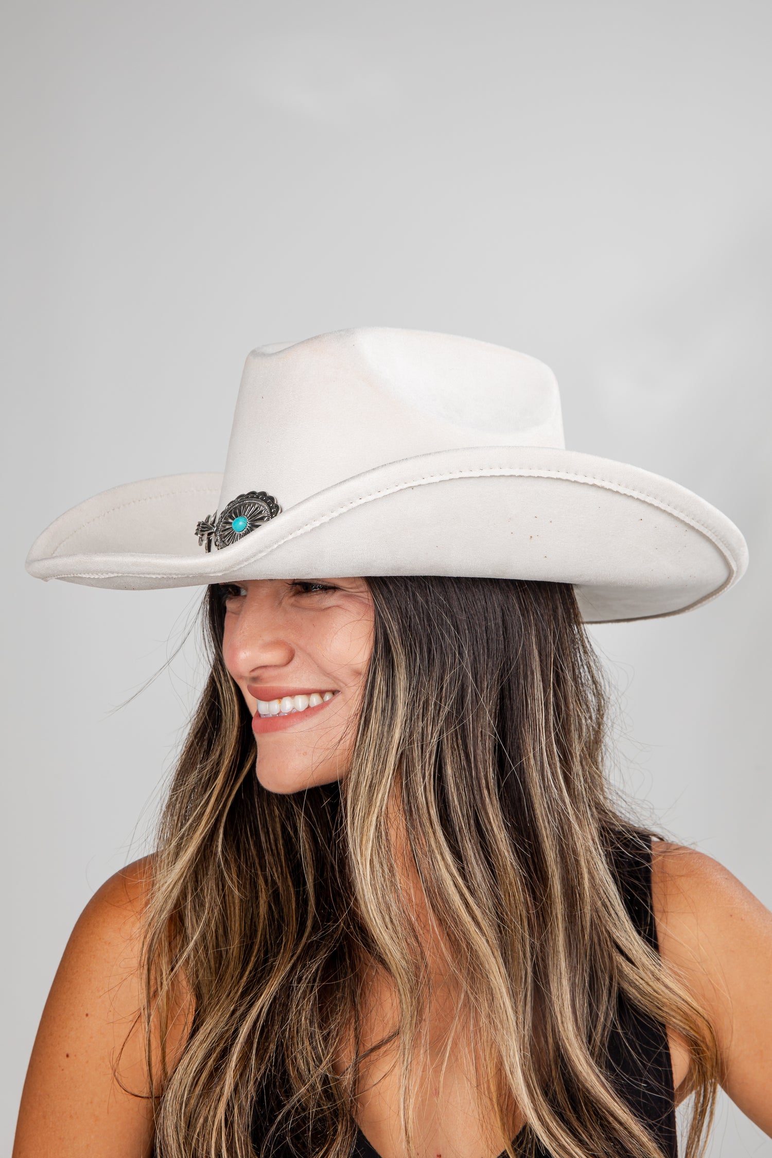 Woman wearing a white cowboy hat with a blue gemstone on a gray background